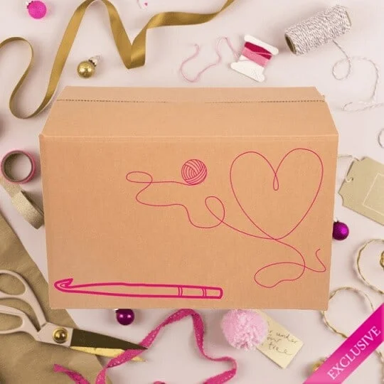 Cardboard box with a ball of yarn and a heart with scissors and thread placed around the box