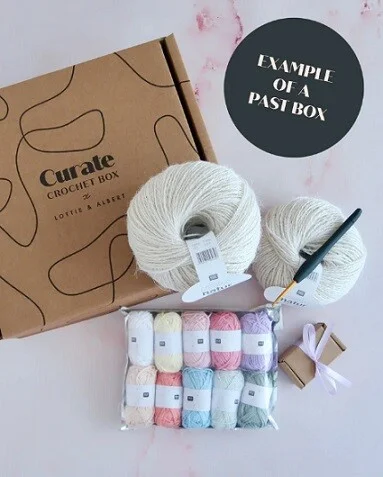 contents from a crochet subscription box includes white yarn, coloured yarn, crochet hook and stitch markers