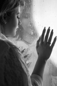Woman leaning against a window with rain drops
