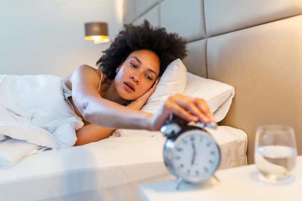 woman in bed turning off alarm clock sleep challenge