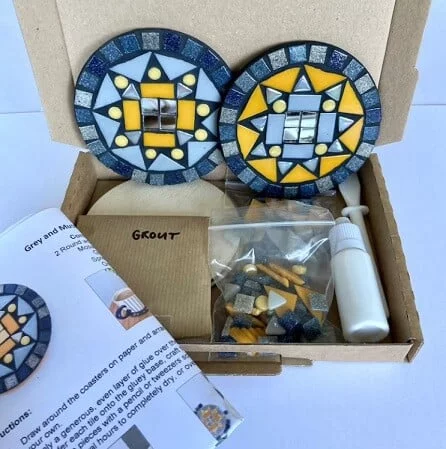 Two mustard and grey mosaic coasters in a box with all the supplies you need to make them