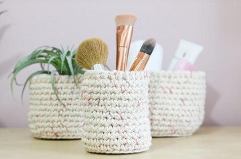 3 crochet nesting baskets, 1 holding beauty brushes, 1 holding makeup tubes, 1 has a plant inside