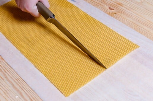 White hand holding a knife to score a piece of beeswax to make a beeswax wrap
