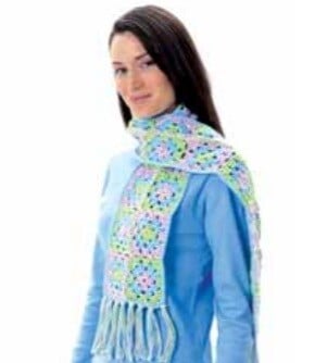 A white darkhaired woman is wearing a crochet scarf and a blue top