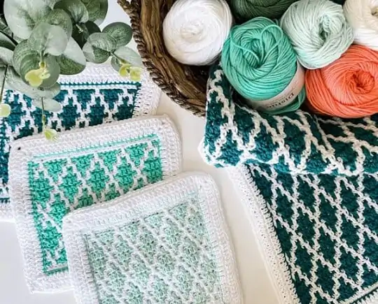 mosaic crochet dishcloths in 3 different shades of blue and a brown bowl which has the balls of yarn in