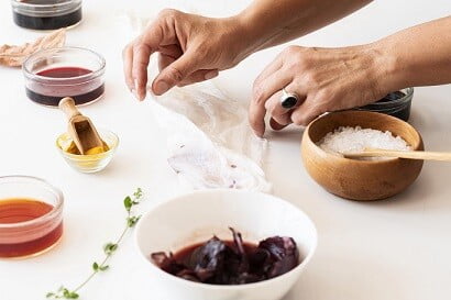 White hands making natural dyes from kitchen ingredients. Bowls of coloured dyes in orange and red with a bowl of bicarbonate of soda