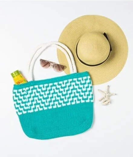 Mosaic crochet tote bag in turqoise and a sunhat and shades to the right of the tote bag