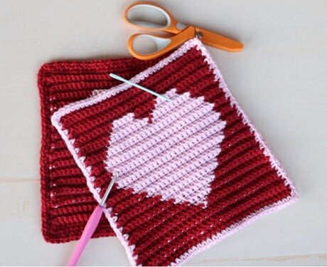 crocheted washcloth in red with a white heart in the centre and a white border