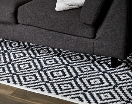 Lattice Tapestry Crochet Rug in black and white on the floor partly beneath a grey sofa