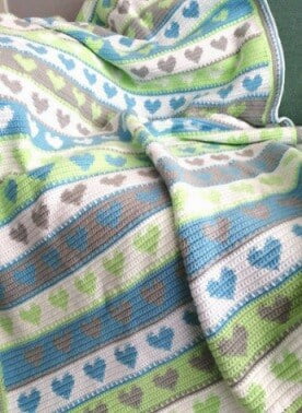crochet blanket in stripes of hearts and block colours in blue, green and grey worked in tapestry crochet technique