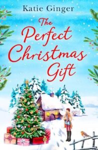 Book Cover for The Perfect Christmas Gift by Katie Ginger. An outdoor snow scene with a cottage in the background, a decorated Christmas tree with presents underneath on the green, a robin perched on a railing and a woman in hat and coat standing by the tree