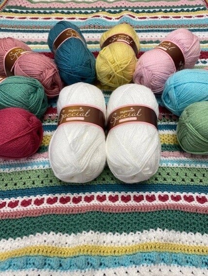 11 different coloured balls of yarn on top of a crocheted blanket