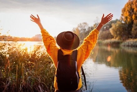 A woman stands with her back to the camera with her arms in the air enjoying being outside in winter