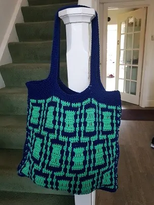 mosaic tote bag in green and blue hanging at the bottom of a staircase in a hallway