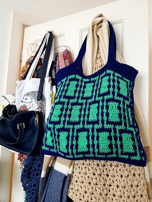 Bags and shawls hanging on the back of a door showcasing a mosaic crochet tote bag in blue and green