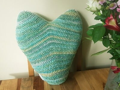 crochet heart pillow in greens and yellows resting on a table