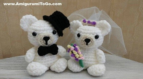 crochet wedding bears in white wearing top hat and bow time and carrying flowers and wearing a veil