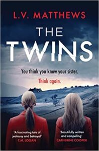 book cover for The Twins by L V Matthews. Two women wearing red jackets look away from the cover to rolling hills