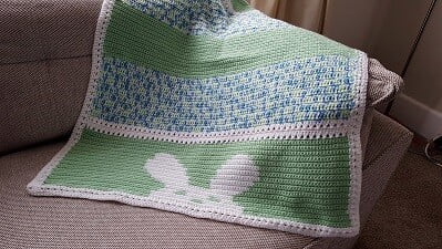 crochet bunny blanket draped over the arm and back of a sofa