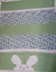 crochet baby blanket with a bunny peeking over the bottom of the blanket