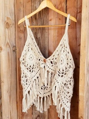 Crochet top made from granny squares in beige yarn hanging on a coat hanger