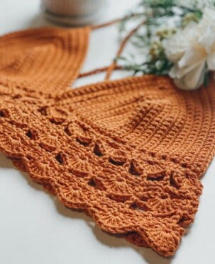 crochet bralette in orange laid flat with a white flower