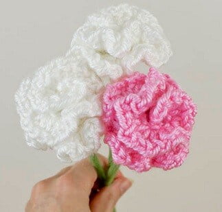 two white crochet carnations and one pink being held by their stems