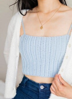 young woman wearing a blue crochet crop top, white cardigan and jeans