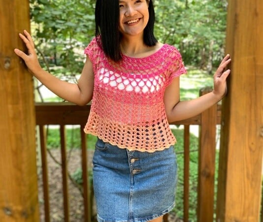 A woman is wearing a pink and peach crocheted lace top paired with a denim skirt