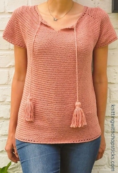 A woman is wearing a salmon coloured crochet top with tassels at the neckline