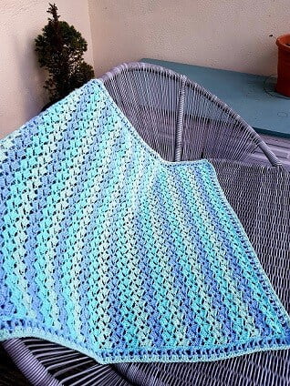 crochet baby blanket in pastel blue and green draped over a garden sofa