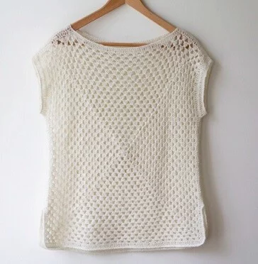 Top crocheted from granny squares in white hanging on a coat hanger