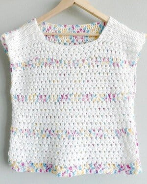 granny stripe crochet top in white with stripes of multi colour hanging on a coat hanger