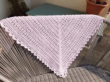 lacy crochet shawl in light pink draped over a chair