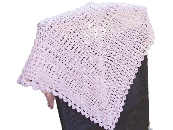 a lacy crochet shawl in pink is draped over the back of a chair