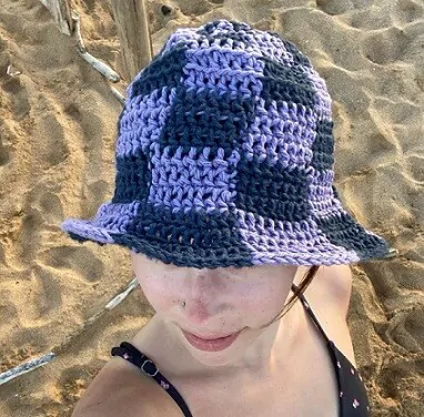 A woman on a beach is wearing a dark blue and light blue checkered sun hat