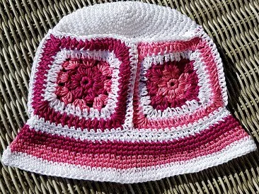 bucket hat crocheted in different shades of pink granny squares, a white crown and a striped brim