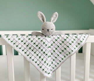 crochet bunny lovey in white and green draped over the side of a white cot