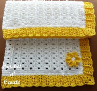 blanket crocheted in white with a sunny yellow border and yellow flower in the corner