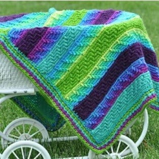 A mosaic crochet baby blanket is draped over a pram