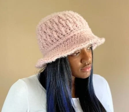 a woman in a white jumper is wearing a pink crocheted bucket hat