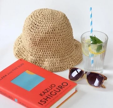 A summer hat is on a table with a book, sunglasses and a cool drink