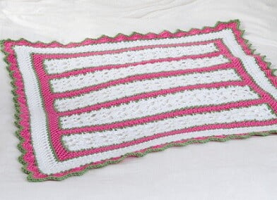 crocheted blanket in pink and white with a green border