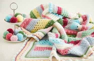 multi coloured crochet blanket with bright coloured pom poms