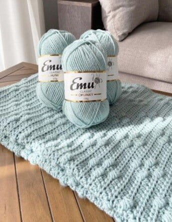 crochet baby blanket in cool blue on a table with balls of the yarn used