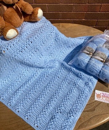 baby blanket crocheted in blue with a teddy sitting on the blanket