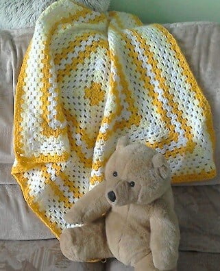 granny square blanket in cream and mustard with a teddy sat on the blanket