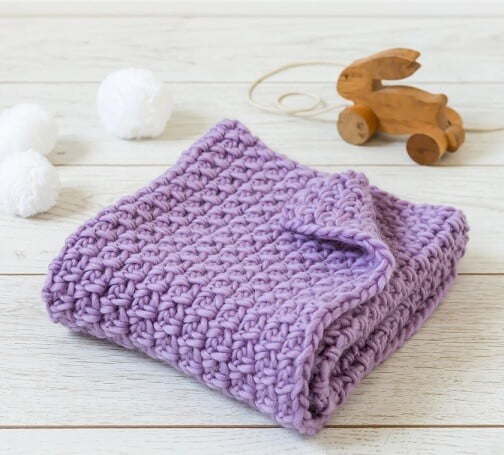 Purple baby blanket folded with a toy dog next to the blanket