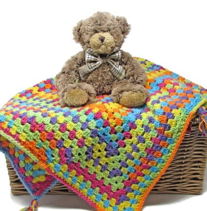 granny square blanket crocheted in rainbow colours with a teddy sat on top of the blanket