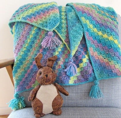 Colours of blue and pastel rainbow in stripes make up this corner to corner baby blanket
